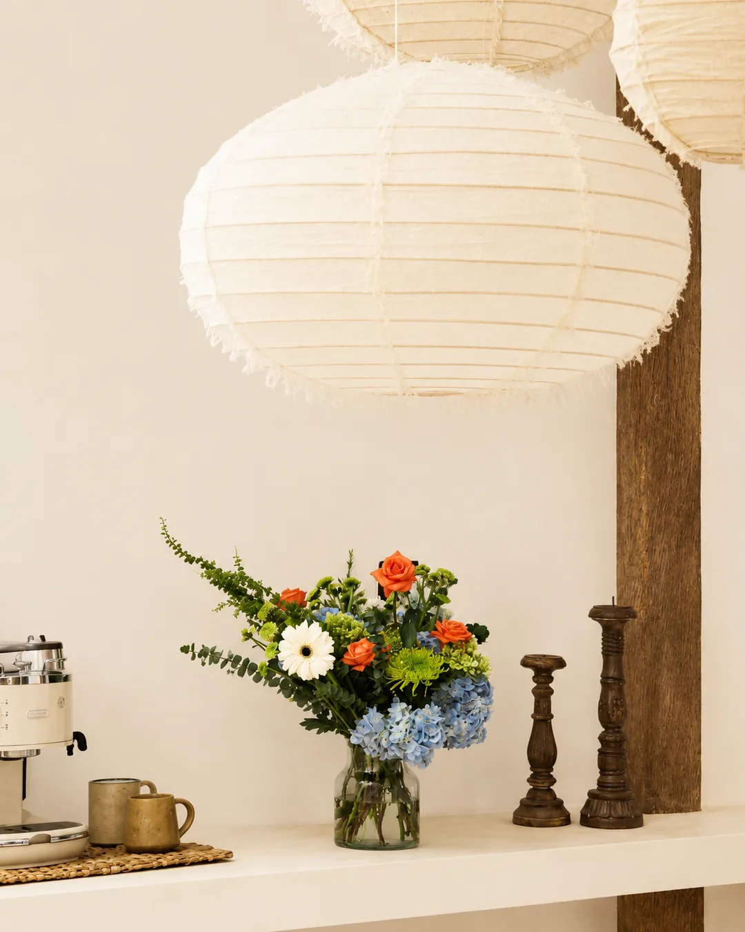 Blue and orange bouquet on a shelf beneath woven paper lanterns